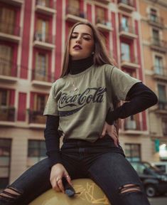 a woman sitting on top of a skateboard in front of a building with her hands on her hips