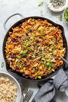 a skillet filled with rice and vegetables on top of a white table next to other dishes