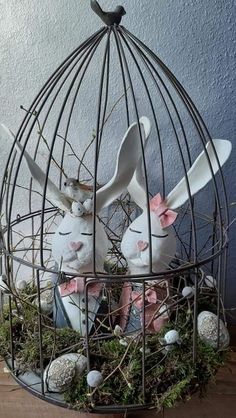 two white rabbits in a birdcage with moss growing on the ground and eggs inside