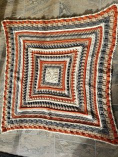 a crocheted blanket is laying on the floor in front of a tile wall