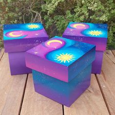 three purple and blue boxes sitting on top of a wooden table with trees in the background