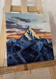 an easel with a painting on it and a mountain in the background at sunset