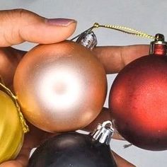 a person holding three different colored christmas ornaments in their hands, one red and one black