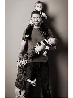 a black and white photo of a man holding two children in his arms while standing against a wall