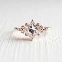 an engagement ring with a princess cut diamond surrounded by smaller round diamonds on a white background