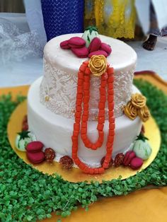 a three tiered white cake with orange and red decorations on the top, surrounded by greenery