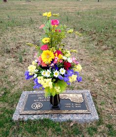 a vase filled with colorful flowers sitting on top of a plaque in the middle of a field