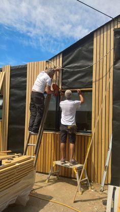 two men working on the side of a building with wood siding and tarp covering it