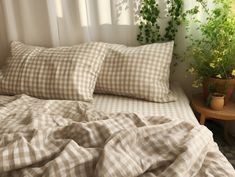 an unmade bed covered in checkered sheets and pillows with potted plants next to it