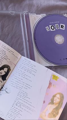 an open cd case sitting on top of a bed next to a book and pen