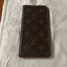 a brown louis vuitton wallet laying on top of a white sheeted bed