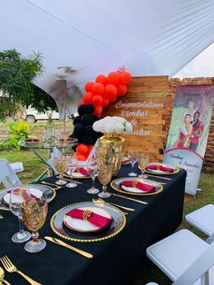 a table set up for an event with black and gold plates, red napkins, and balloons