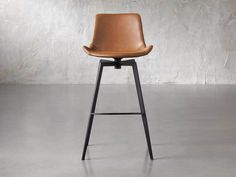 a brown leather bar stool sitting on top of a cement floor next to a white wall