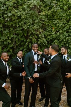 a group of men standing next to each other in front of a lush green wall