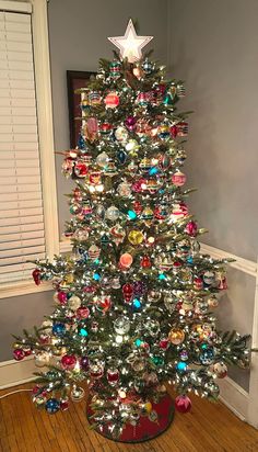 a decorated christmas tree in a room with wooden flooring and white shuttered windows