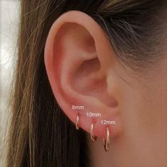 a woman's ear is shown with two small gold hoop earrings