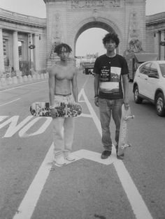 two young men standing in front of an arch with their skateboards on the street