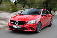 a red mercedes cla driving down a road with trees in the backgroud