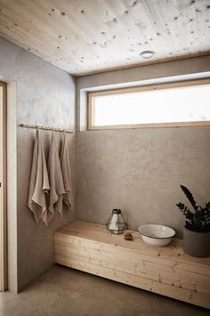 a wooden bench in a bathroom with towels hanging on the wall and a potted plant next to it