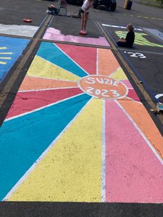 children are playing in the parking lot painted with chalk and sidewalk paint, while an adult sits on his skateboard