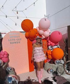 a woman in a pink dress and hat standing next to giant balloons at an event