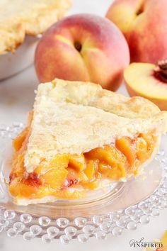 a piece of pie sitting on top of a glass plate next to two peaches