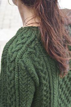 a woman with long red hair wearing a green sweater and looking off into the distance