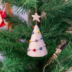 a ceramic christmas tree ornament hanging from a pine tree