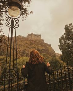 a woman standing in front of a street light with a castle on the hill behind her