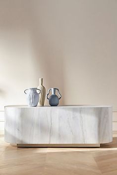 two vases sitting on top of a marble table in front of a white wall