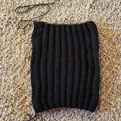 a black knitted bag sitting on top of a carpet next to a string and scissors