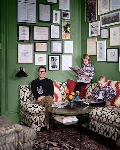 a man and two children sitting on a couch in front of a wall with pictures