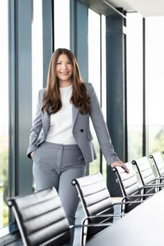 a woman in business attire standing next to a row of empty chairs and looking at the camera