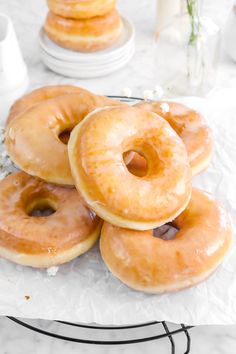 a pile of glazed donuts sitting on top of a white table next to plates