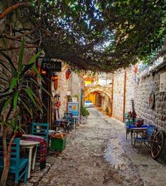 an alley way with tables and chairs on the side, surrounded by vines and trees