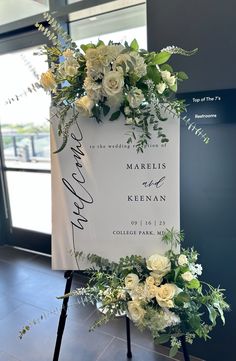 a sign with flowers and greenery on it in front of a window at an event