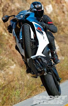 a man riding on the back of a blue and white motorcycle down a hill side