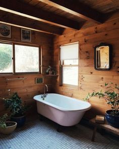 a bathtub in a bathroom with wooden walls and flooring, along with potted plants