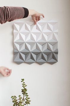 a woman is pointing at an origami piece on the wall next to a plant