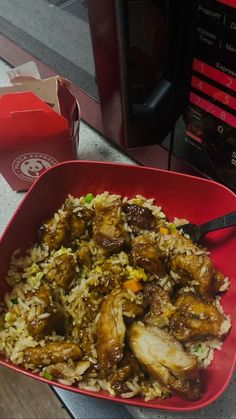 a red bowl filled with rice and meat on top of a table next to a drink