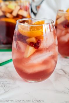 two glasses filled with fruit and ice on top of a marble countertop next to a potted plant