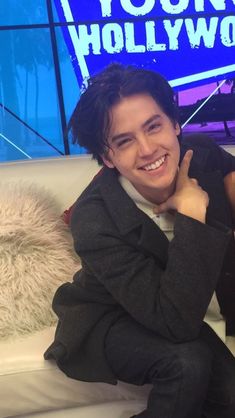 a man sitting on top of a white couch in front of a tv screen with the hollywood sign behind him