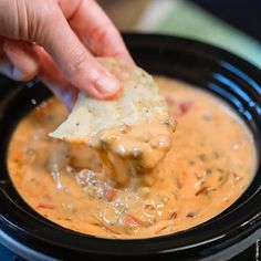 a hand dipping a tortilla chip into a slow cooker filled with soup