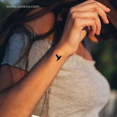 a woman's arm with a small black bird tattoo on the left side of her wrist