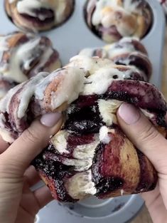 a person holding a pastry in front of some muffins