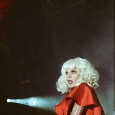 a woman with blonde hair and fishnet stockings on, standing in front of a stage