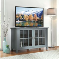 a flat screen tv sitting on top of a wooden cabinet in front of a window