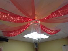 a chandelier hanging from the ceiling with red and white sheers on it