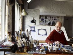 an older man sitting at a table with paint and brushes