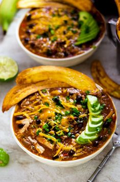 two bowls filled with chili and bananas next to some lime wedges on the side